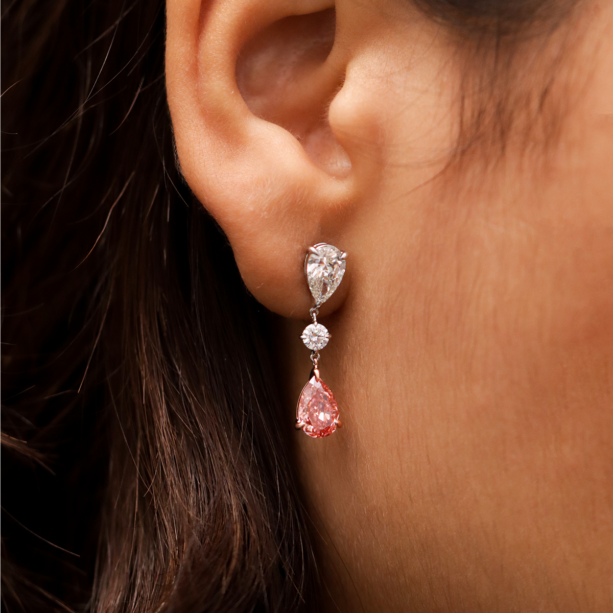 Close-up of an ear wearing a diamond earring with a pink teardrop gemstone. | Pear-Shaped Red Diamond Drop Earrings | Earthly Jewels